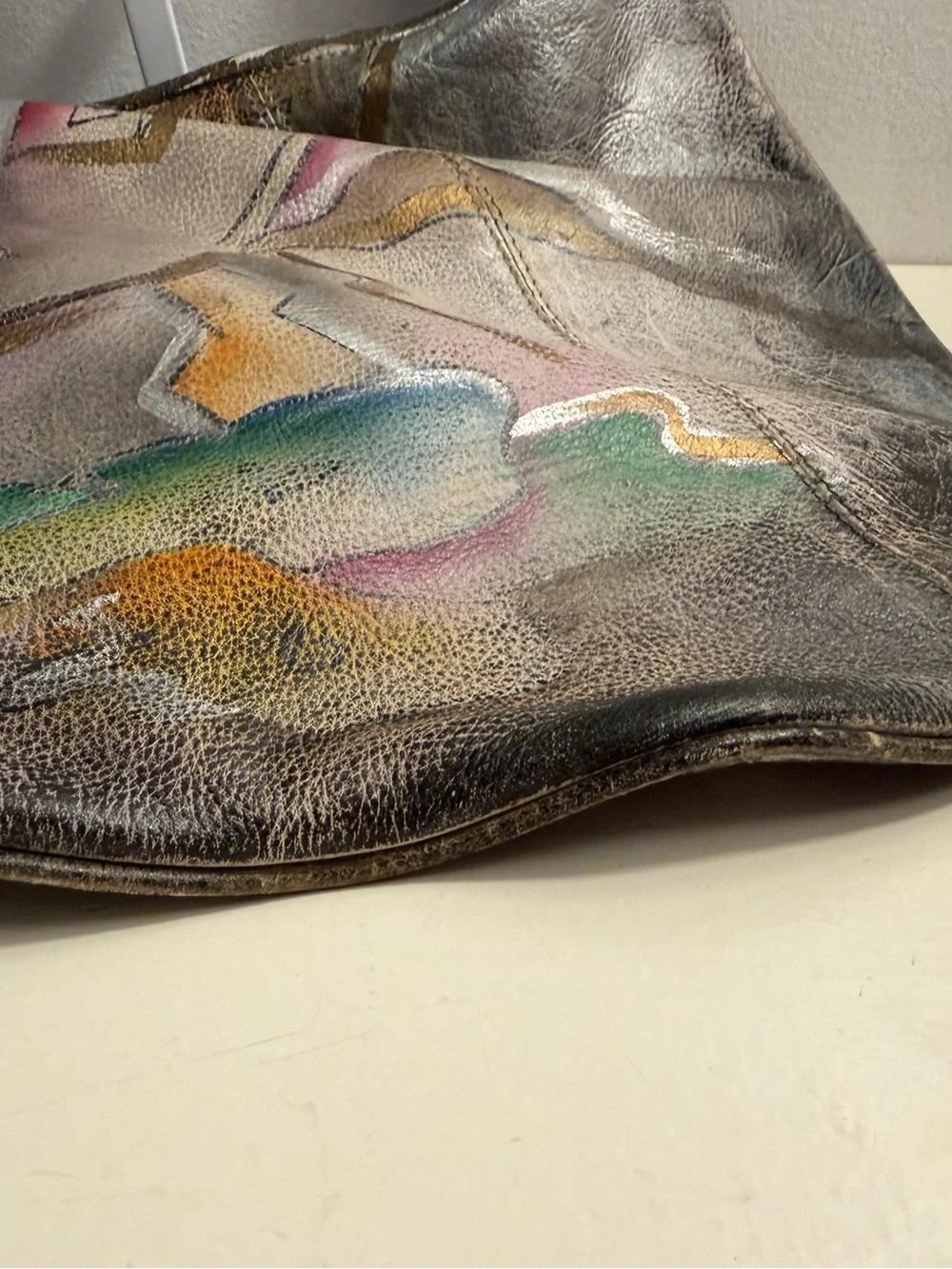 Distressed leather hobo bag with colorful abstract design on front and back.
